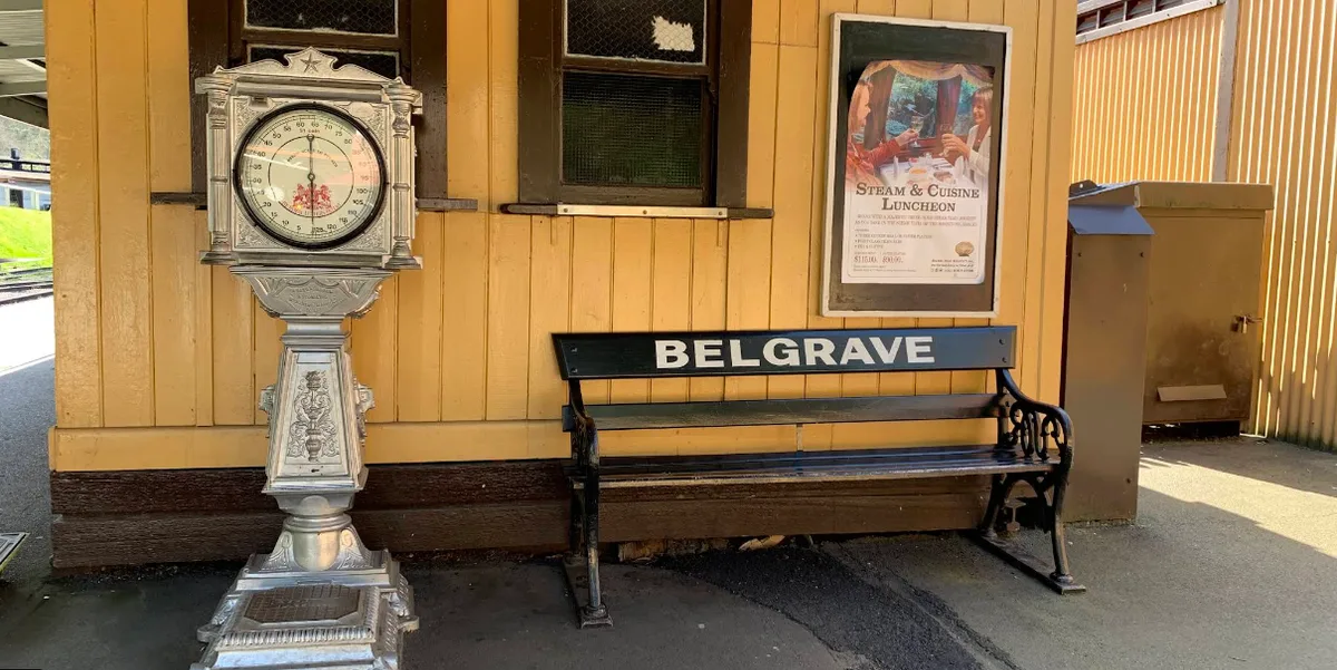 Vintage silver penny scale and black wooden bench stenciled Belgrave against a yellow timber platform wall.
